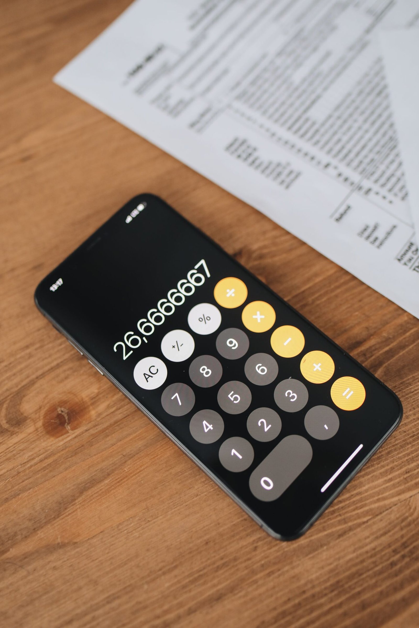 Smartphone calculator app beside financial documents on a wooden desk